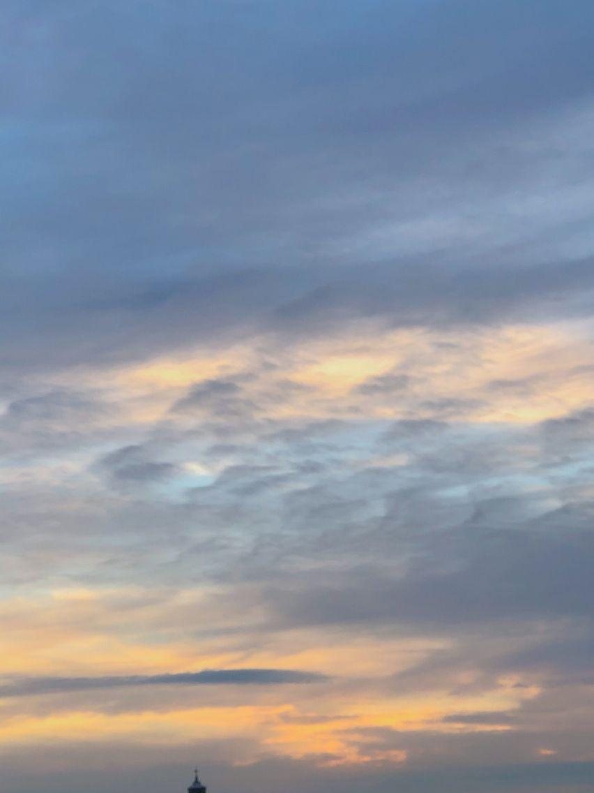 Cielo al atardecer con nubes grises y doradas y la punta de un campanario asomando abajo